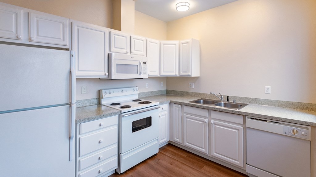 A white kitchen with a refrigerator, stove, oven, microwave, and cabinets.