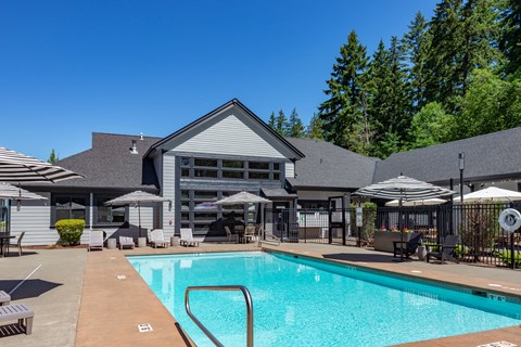A large swimming pool in front of a house with a patio and umbrellas.