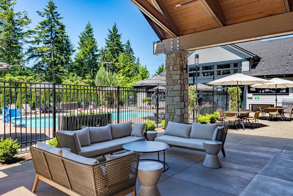 A patio with a sofa, chairs, and a table with a pool in the background.