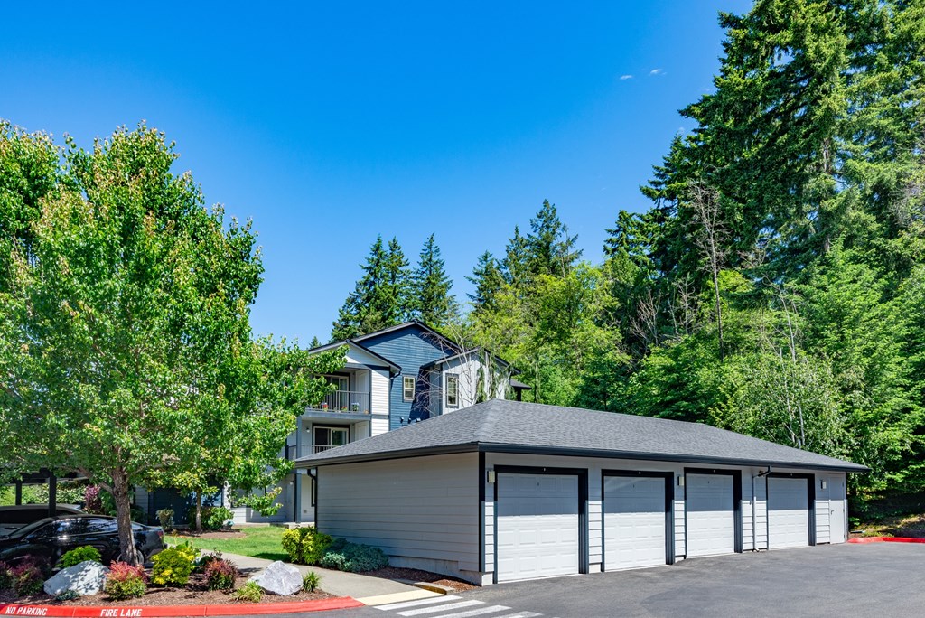 A house with a grey garage door is surrounded by greenery.