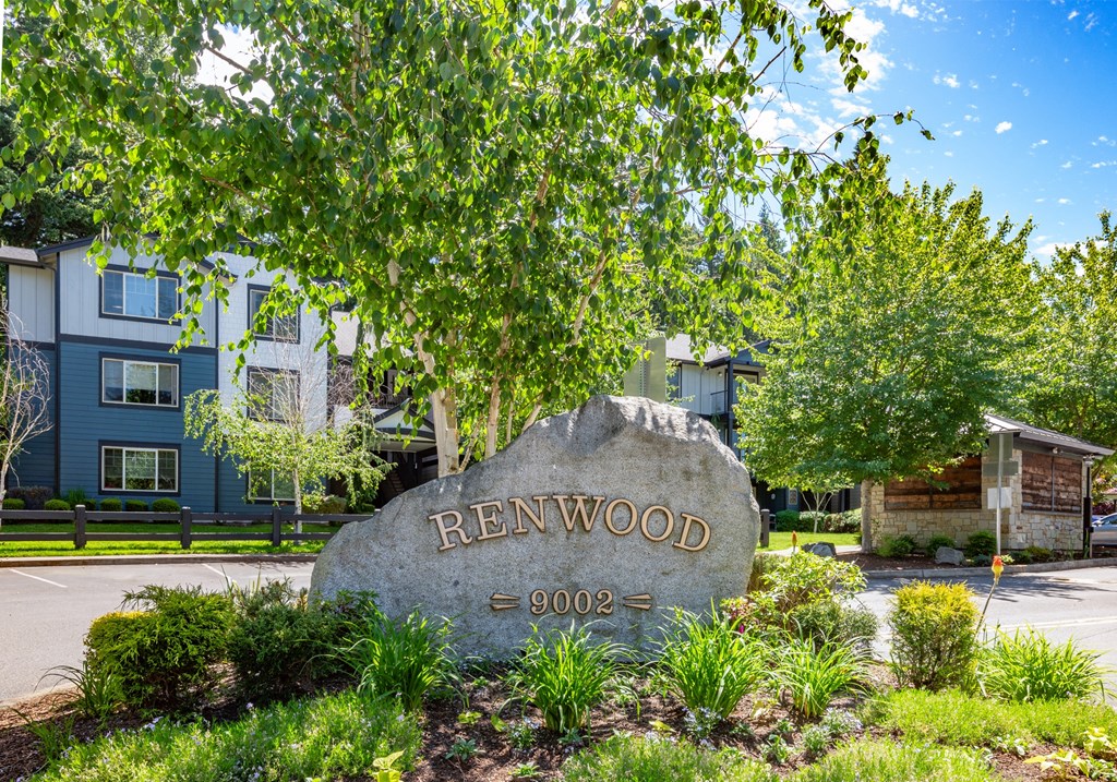 A stone sign with the word RENWOOD and the year 1900 is in the foreground of a well-kept lawn.