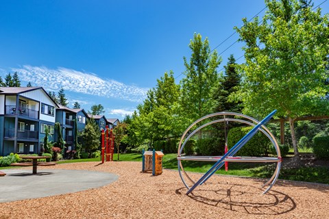 A playground with a large metal ring structure in the foreground and apartment buildings in the background.