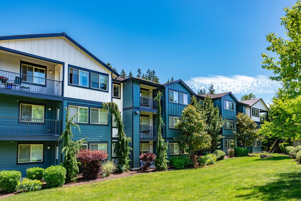 A row of apartment buildings with green bushes in front.