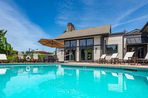 A large swimming pool in front of a house with a sun lounger.