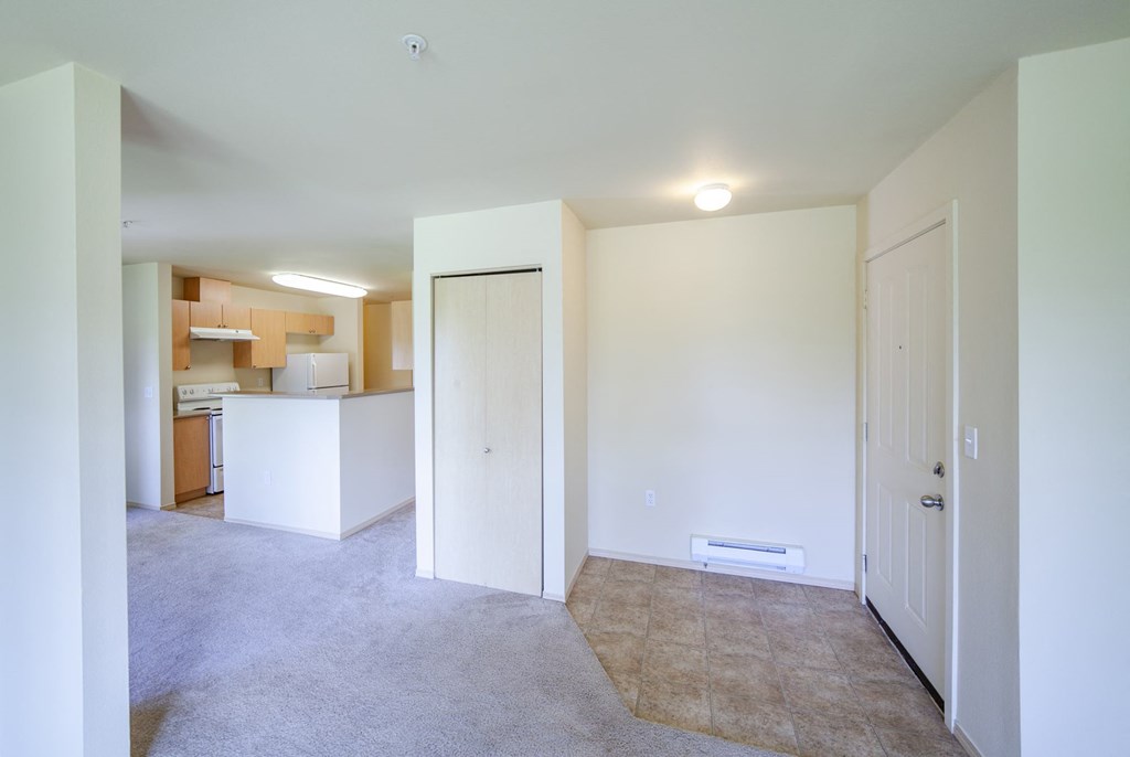 an empty living room with a kitchen in the background