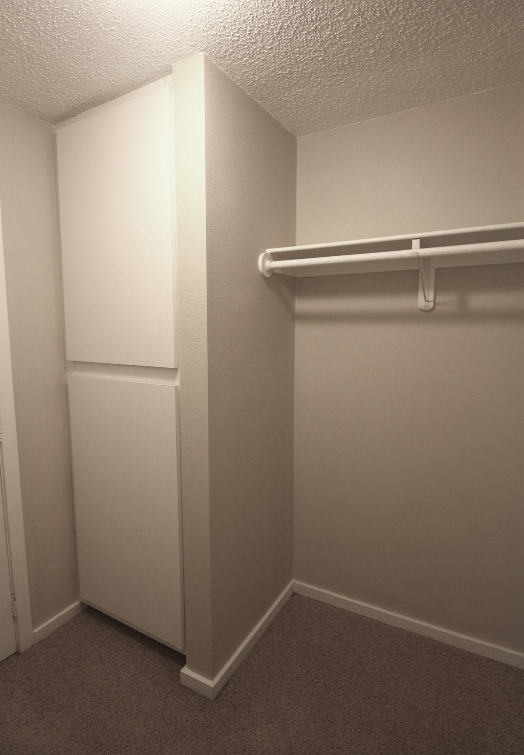 a walk in closet in a room with a white wall and a white refrigerator