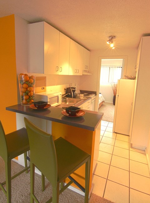 a kitchen with white cabinets and a counter with two green chairs