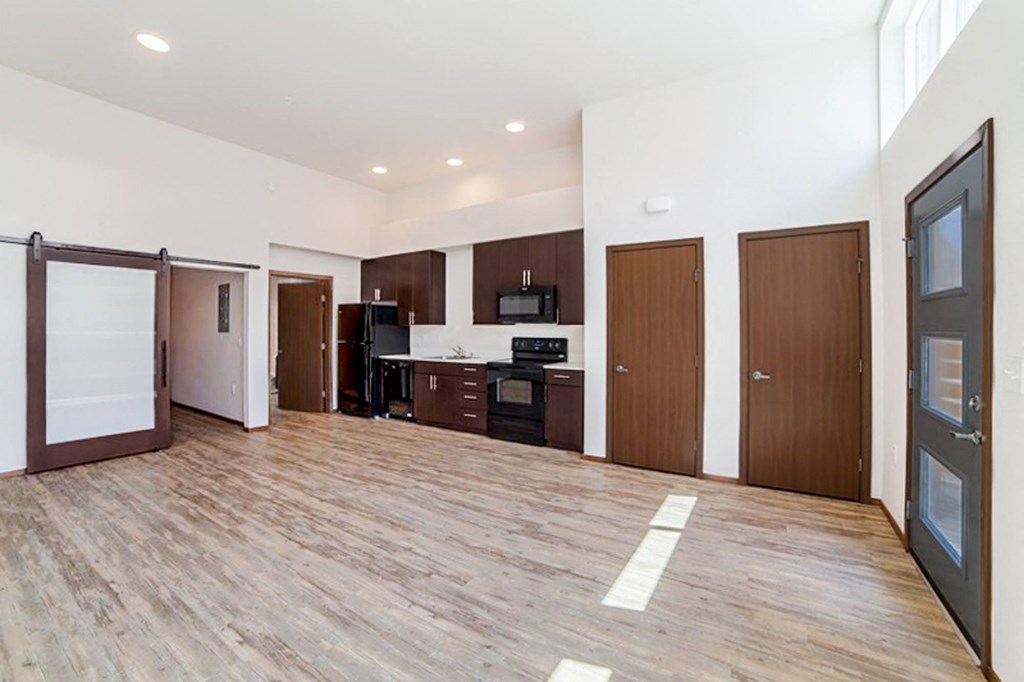 an empty living room and kitchen with wood flooring and white walls