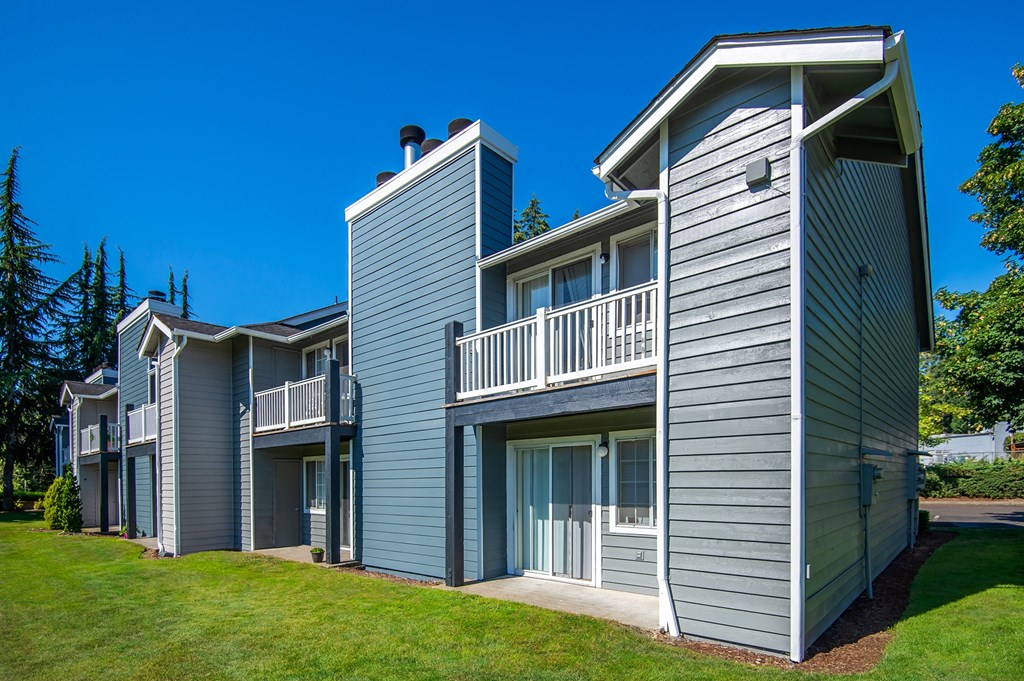 a row of apartments with grey siding and green grass