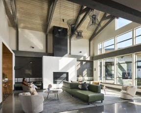 a woman sits on a couch in a large living room with a fireplace and large windows