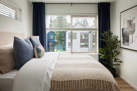 A bedroom with a large bed and a view of a blue house through the window.