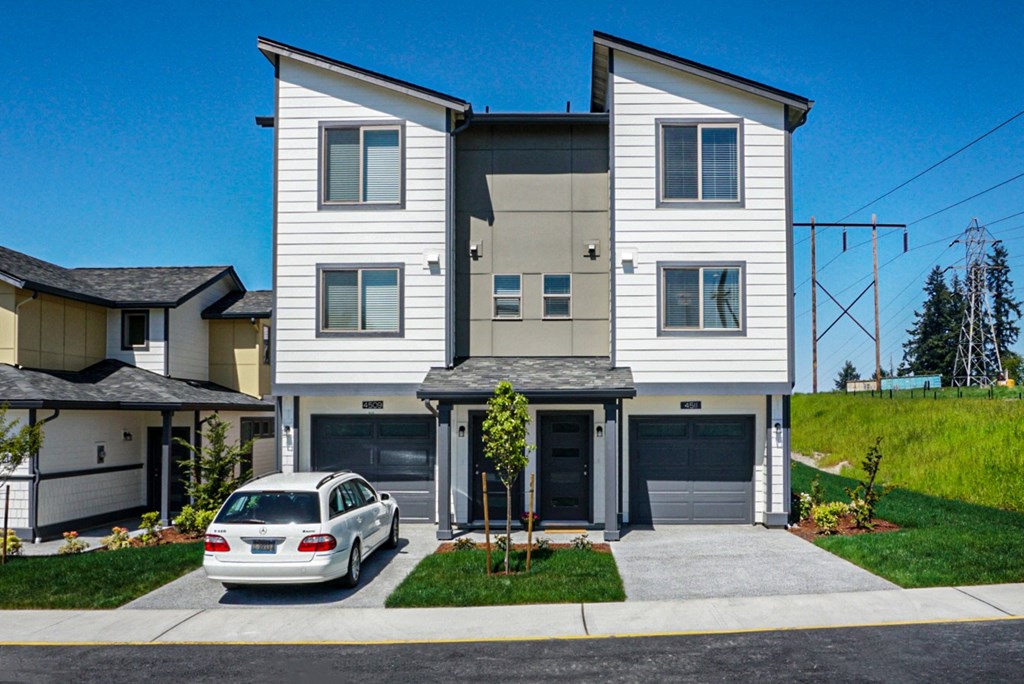 A white house with a grey garage door and a silver car parked in front.