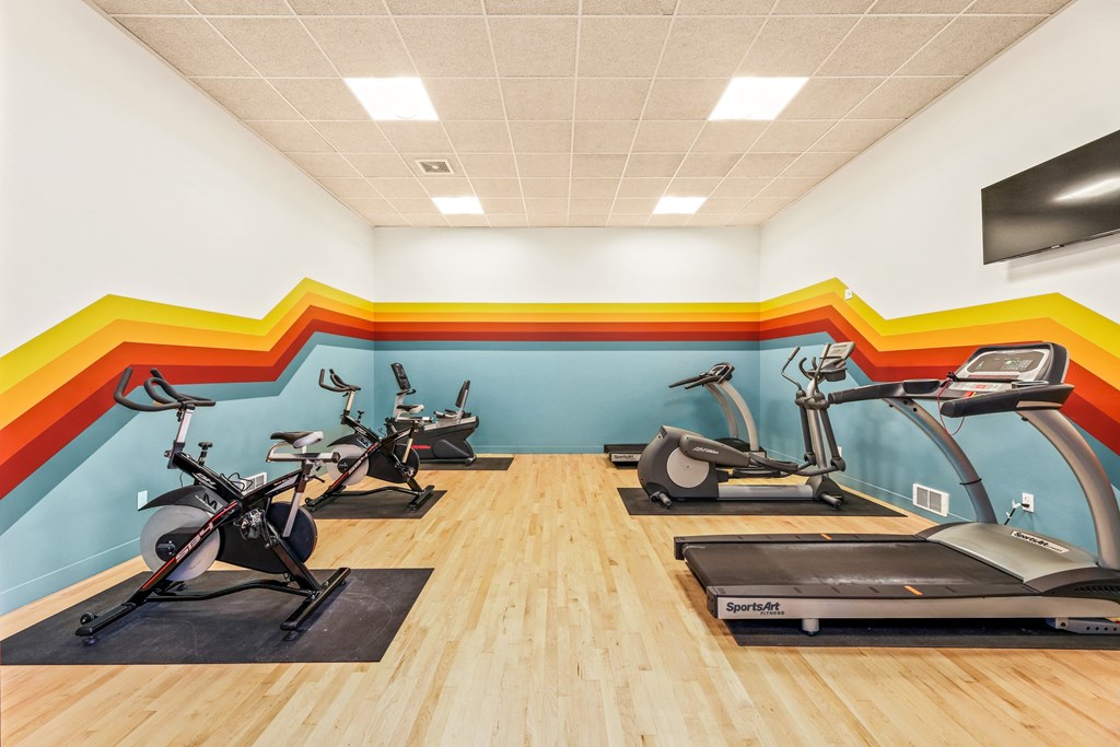 a gym with treadmills and exercise bikes and a wall with a rainbow mural