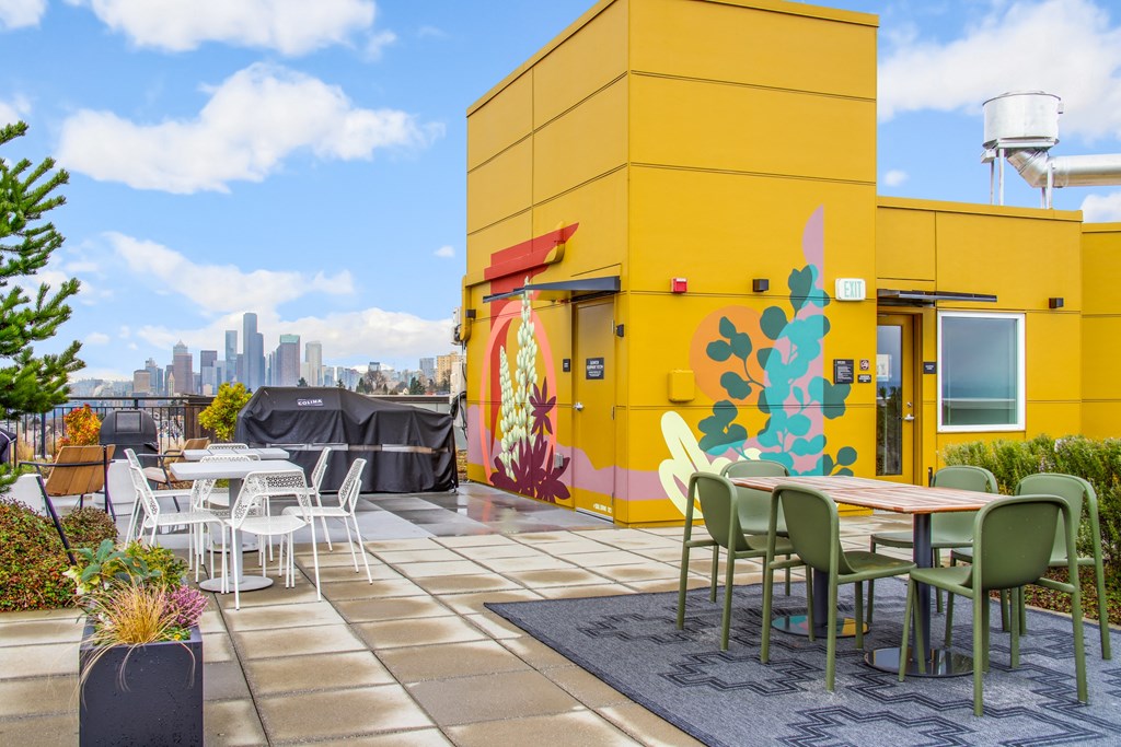 a patio with tables and chairs and a yellow building with a city in the background