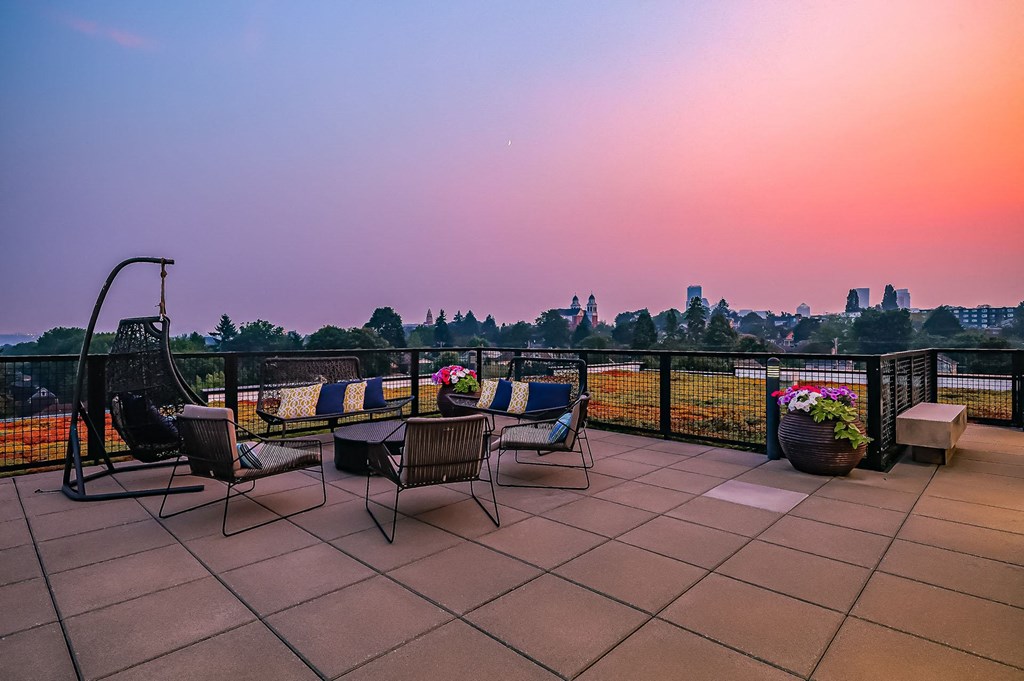 A patio with chairs and a table overlooking a city skyline at sunset.