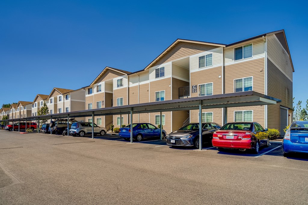 A parking lot in front of a multi-story apartment building with cars parked.