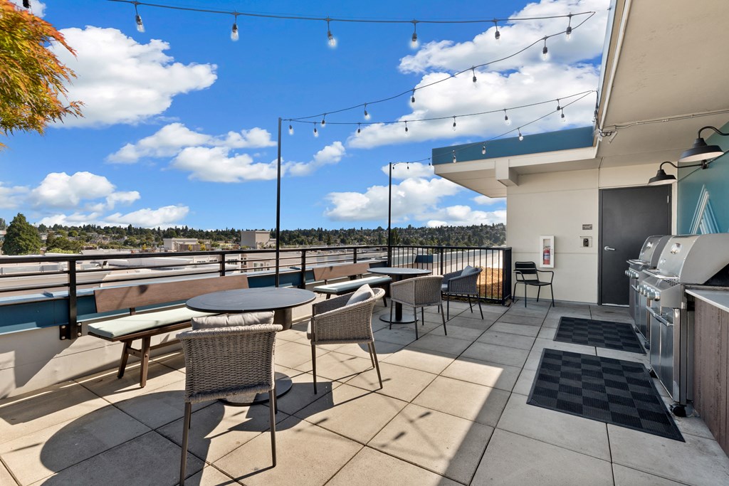 a patio with tables and chairs and a barbecue grill on the side of a building