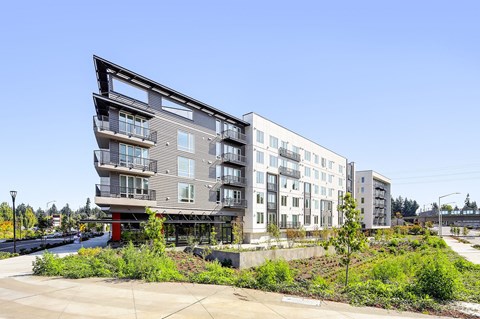 A modern multi-story apartment building with balconies and a landscaped area in front.