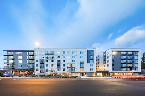 A modern apartment building with multiple balconies and bright lights on the ground floor.