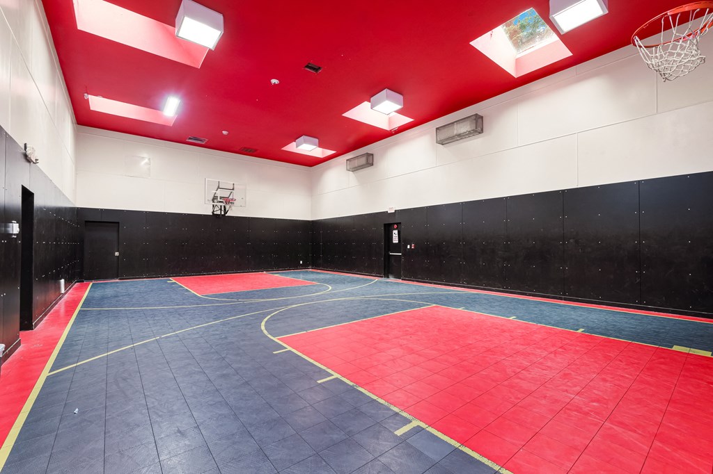 a basketball court in a gym with a red and black wall and blue flooring