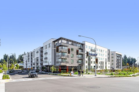 A street view of a modern apartment complex with cars driving on the road.