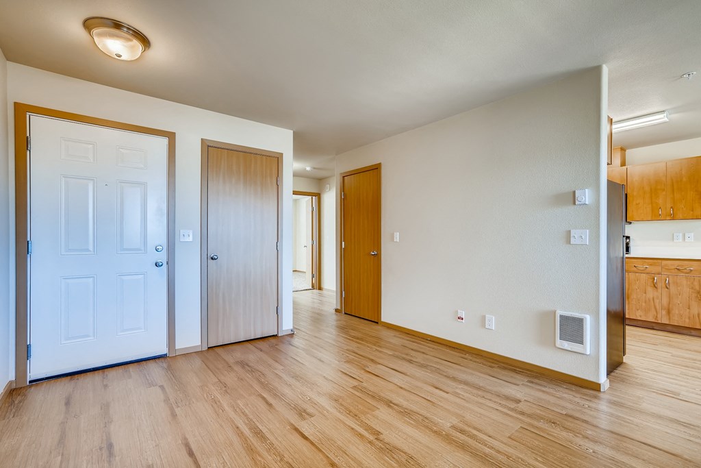 A room with wooden floors and white walls with a door on the left and a cabinet on the right.