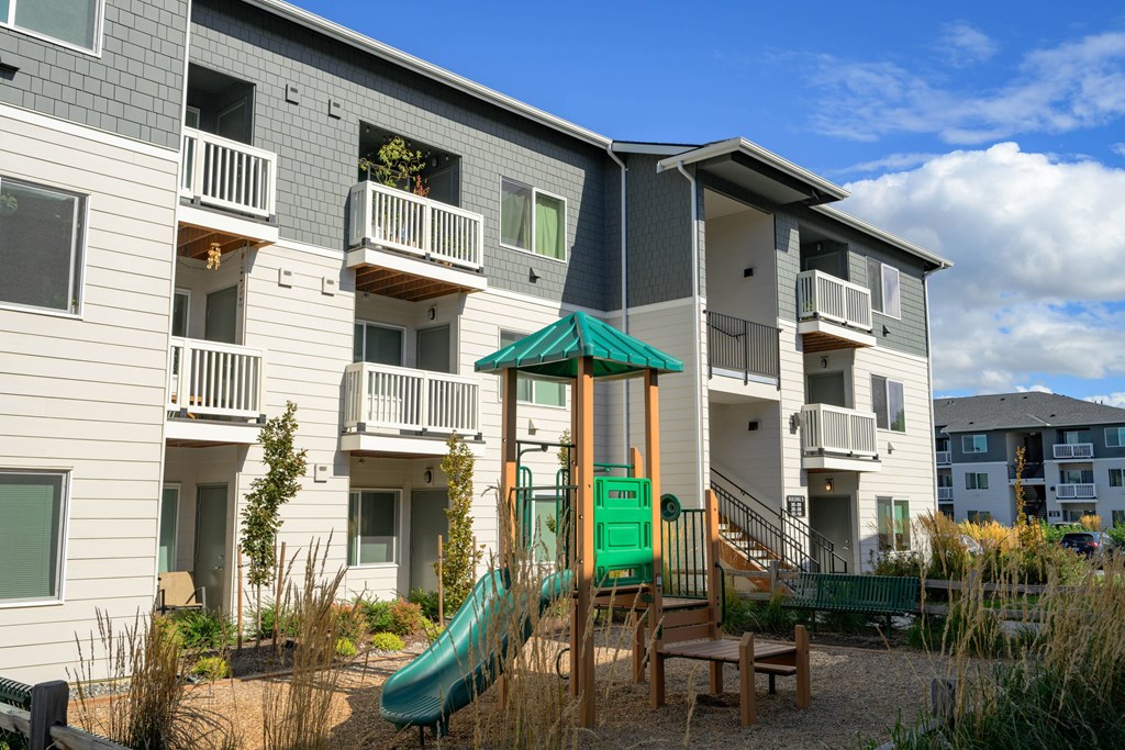 A playground area with a green slide in front of apartment buildings.