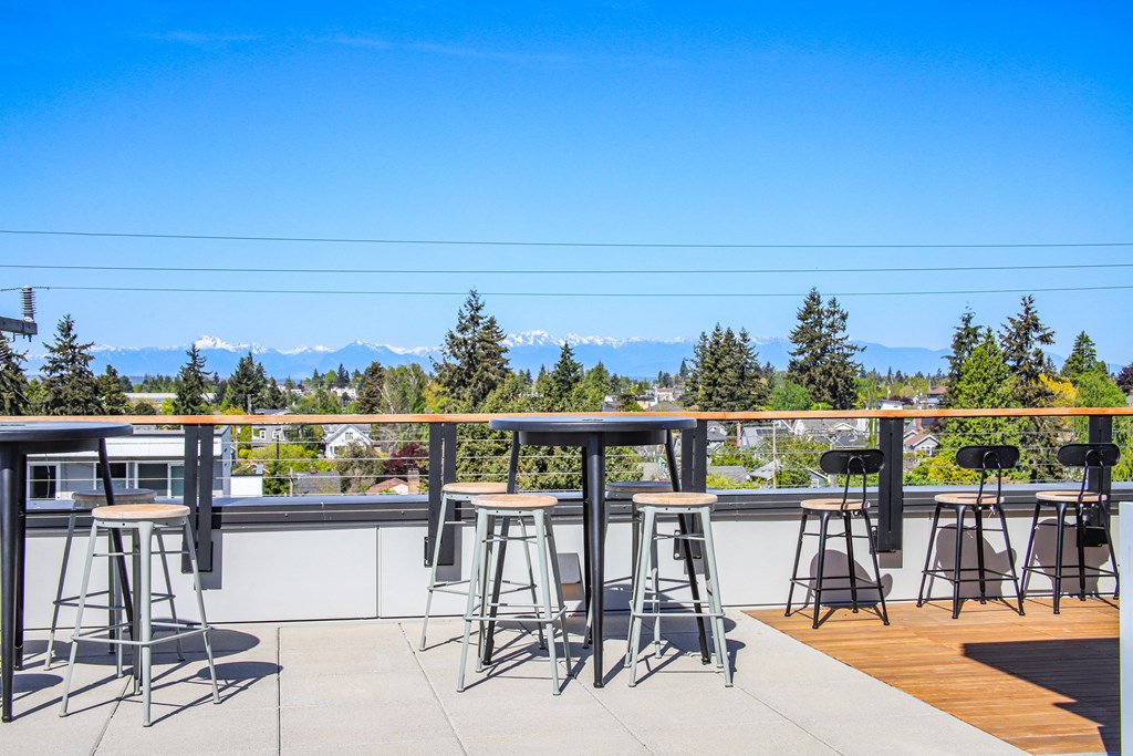 a rooftop bar with bar stools and tables with mountains in the background