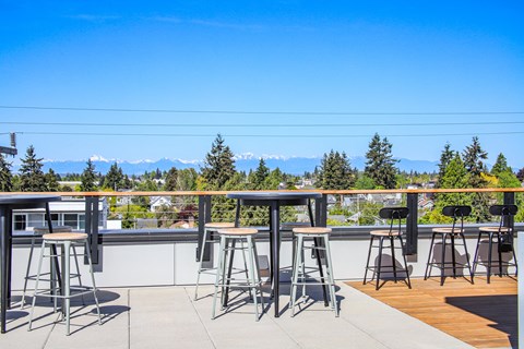 a rooftop bar with bar stools and tables with mountains in the background