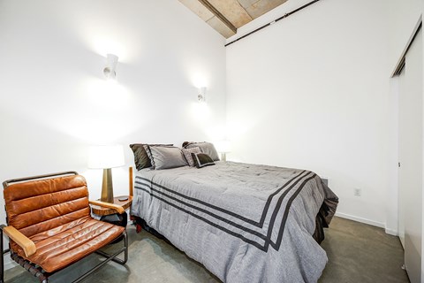 A bedroom with a bed, a chair, and a lamp.