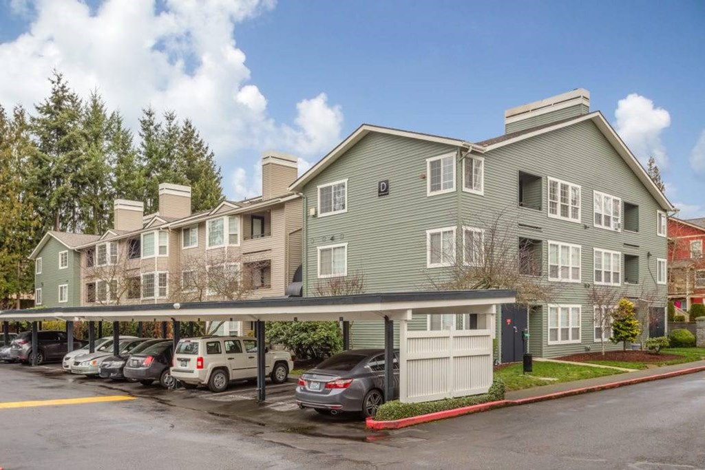 A row of cars are parked in a parking lot in front of a building.