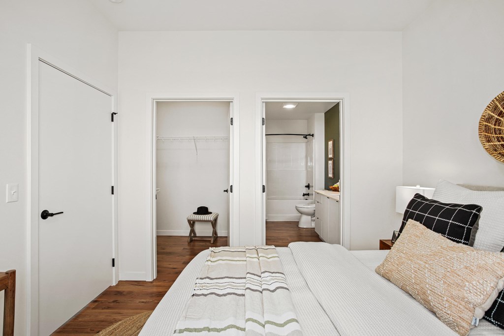 A white bedroom with a bed, a chair, and a wicker basket on the wall.