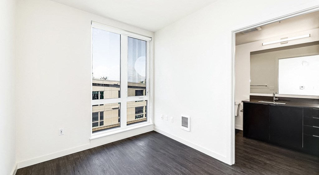 an empty living room with a large window and a kitchen