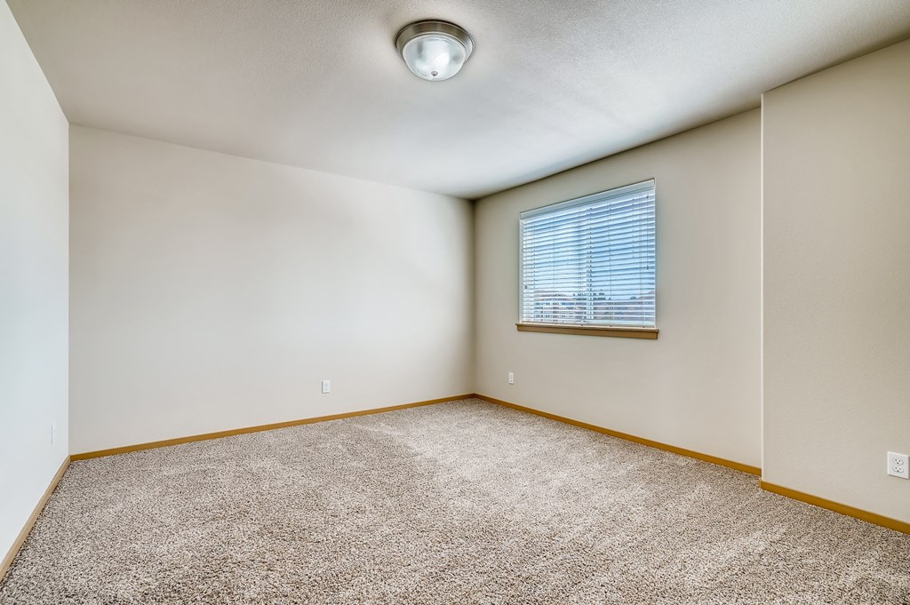 A room with a carpeted floor and a window with blinds.