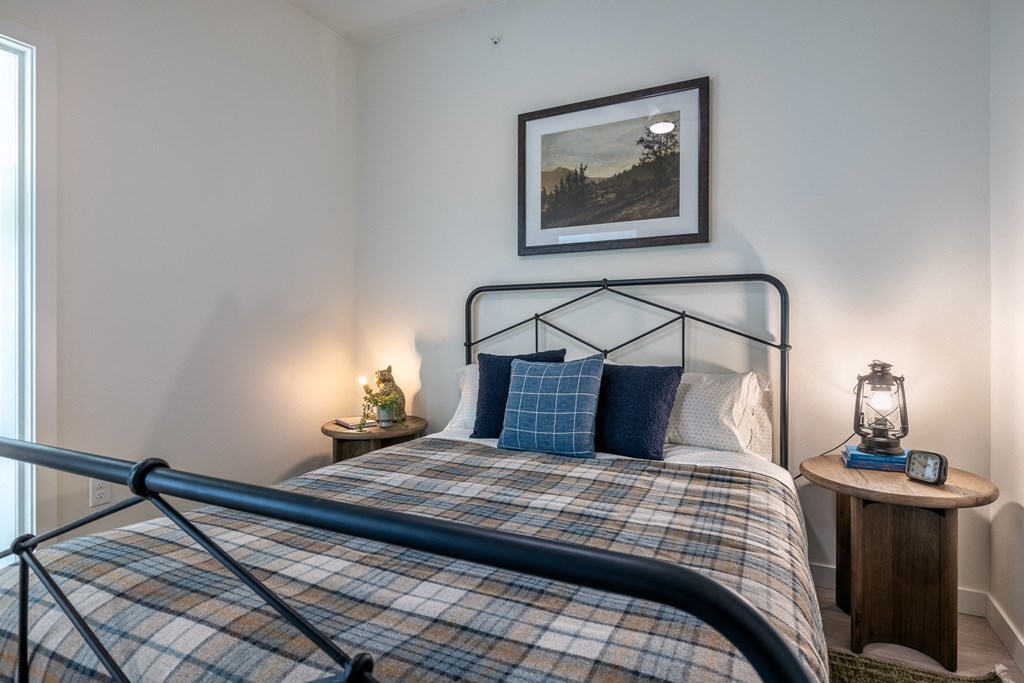 A bed with a plaid comforter and a lantern on a side table.
