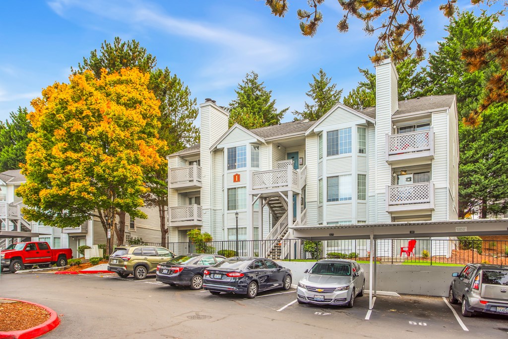 A row of cars are parked in a parking lot in front of a building.