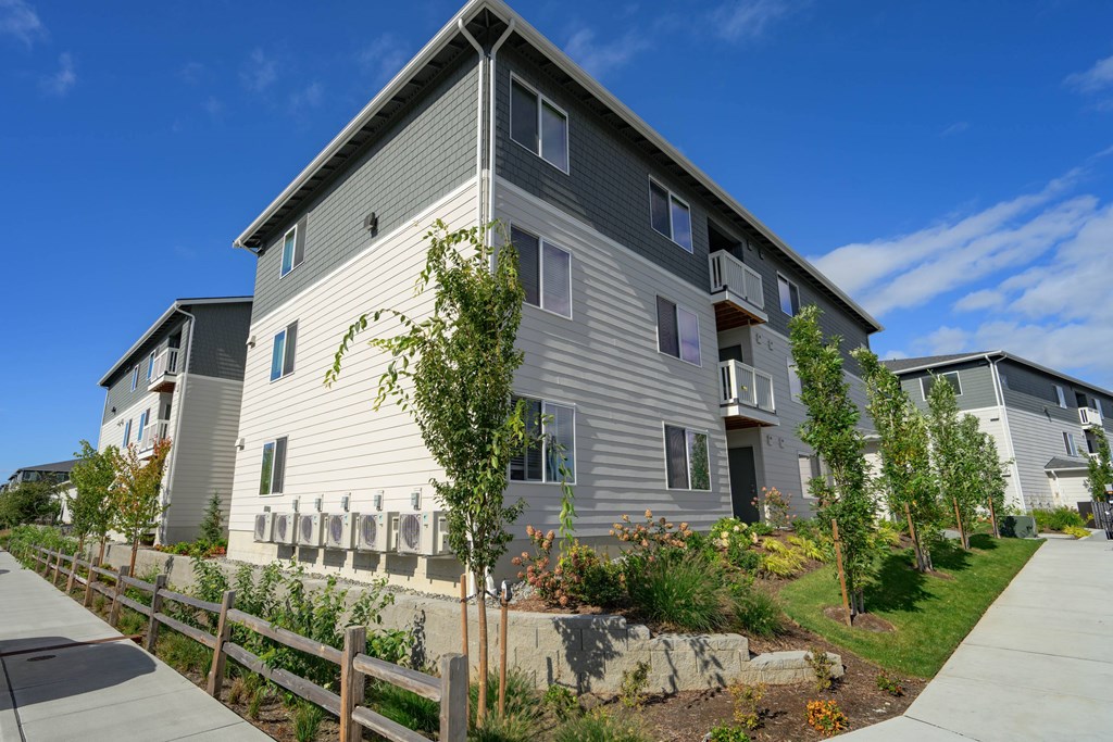 A modern two-story building with a grey exterior and a well-maintained garden in front.