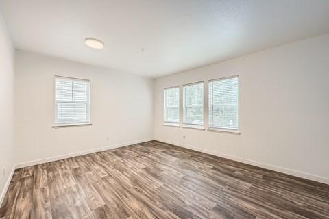 A room with wooden flooring and three windows.