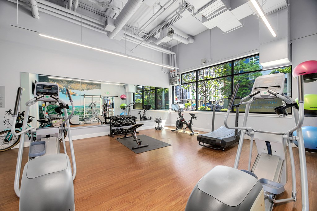 a gym with exercise equipment and windows in a room with wood floors