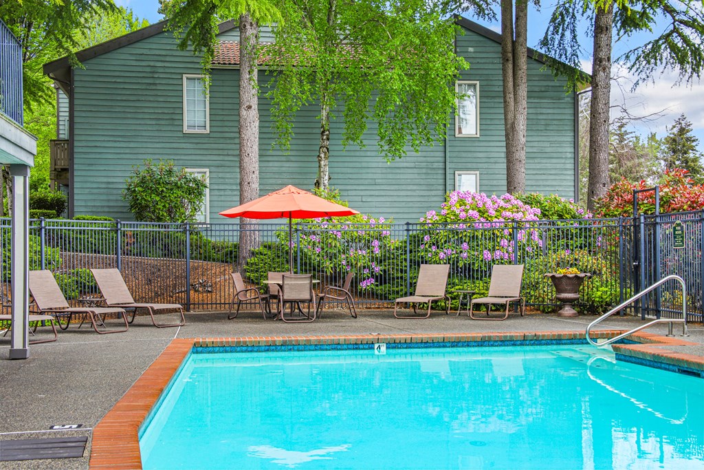 a swimming pool with chairs and an umbrella in front of a house