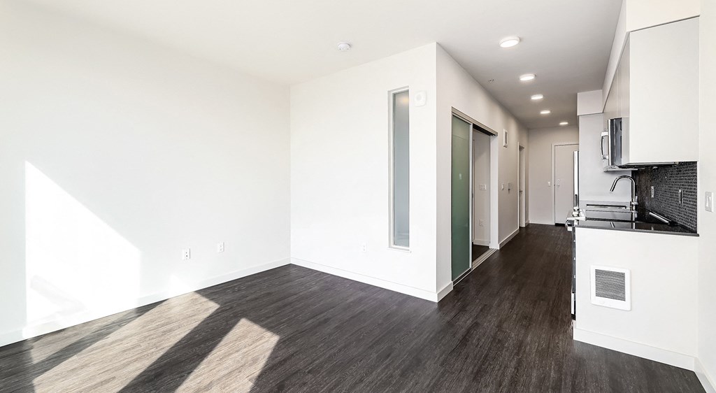 a living room and kitchen with white walls and wood flooring