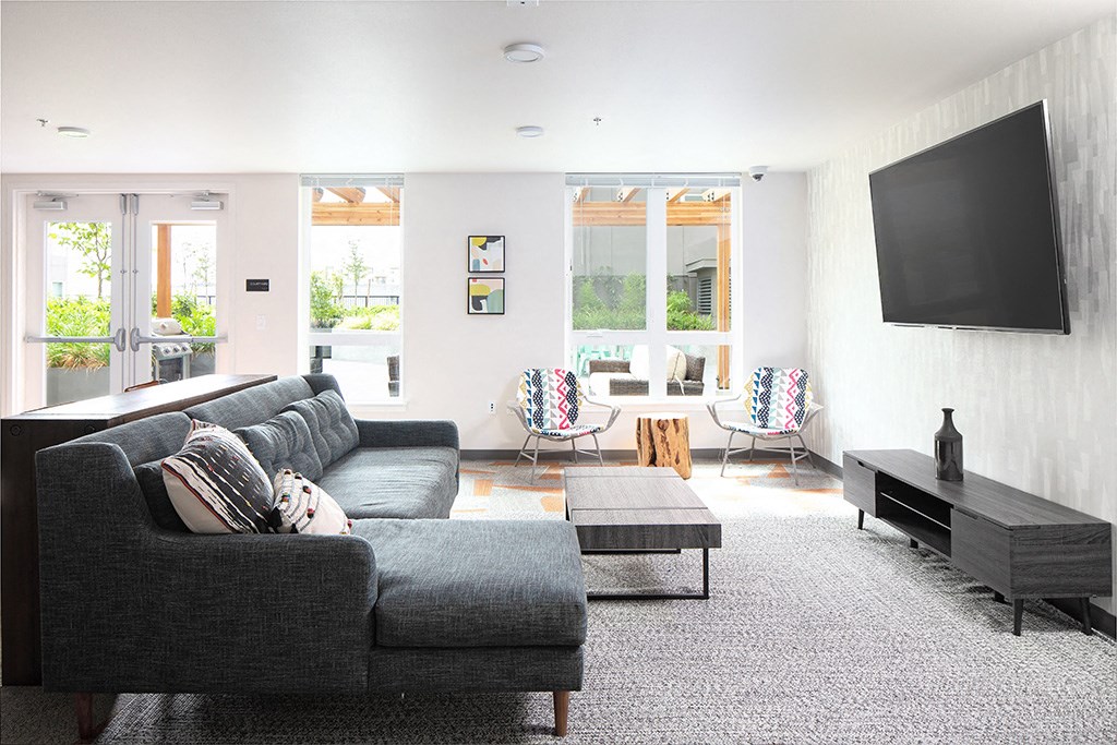 a living room with white walls and grey couches with a flat screen tv on the wall