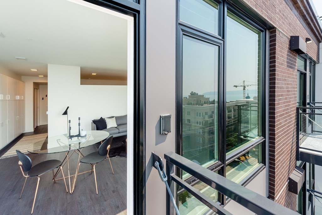 a balcony with a glass table and chairs and a large window with a view of the city