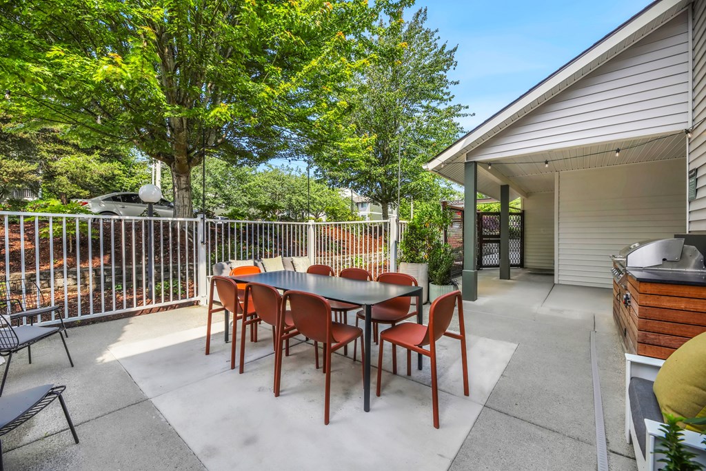 A patio with a table and chairs is surrounded by a fence and trees.