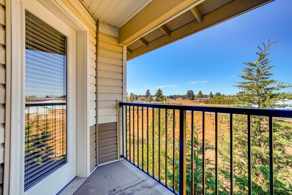 A balcony with a black railing and a view of a field and trees.