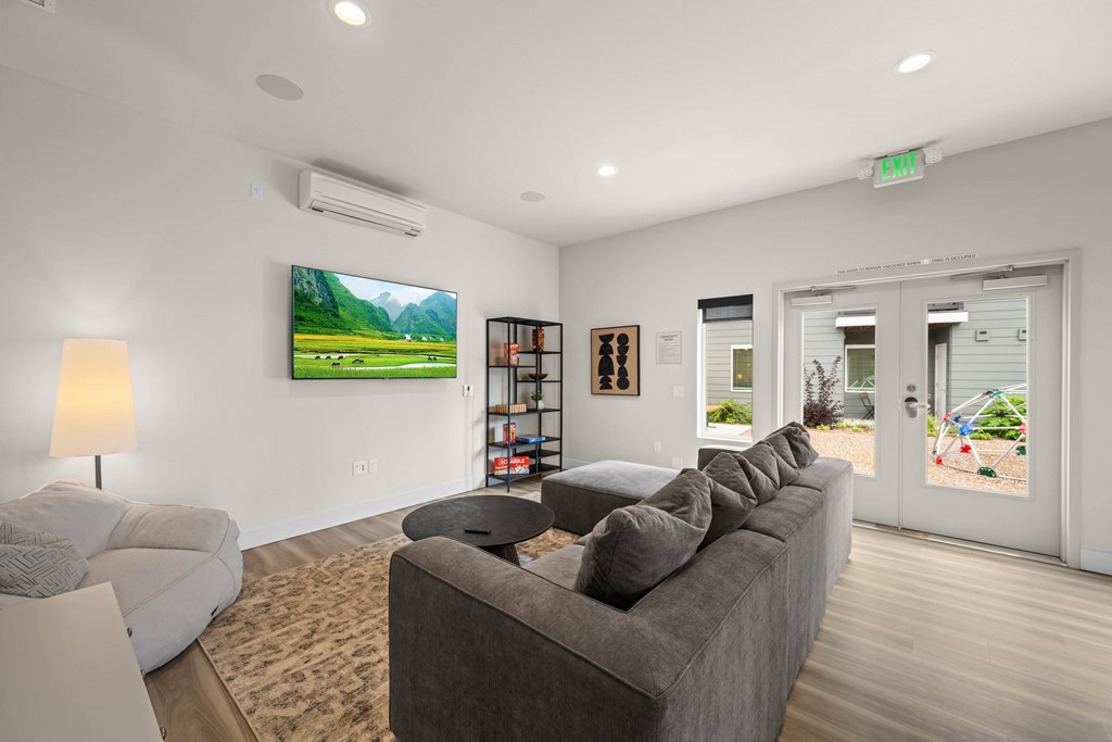 A living room with a grey couch and a painting of a green landscape on the wall.