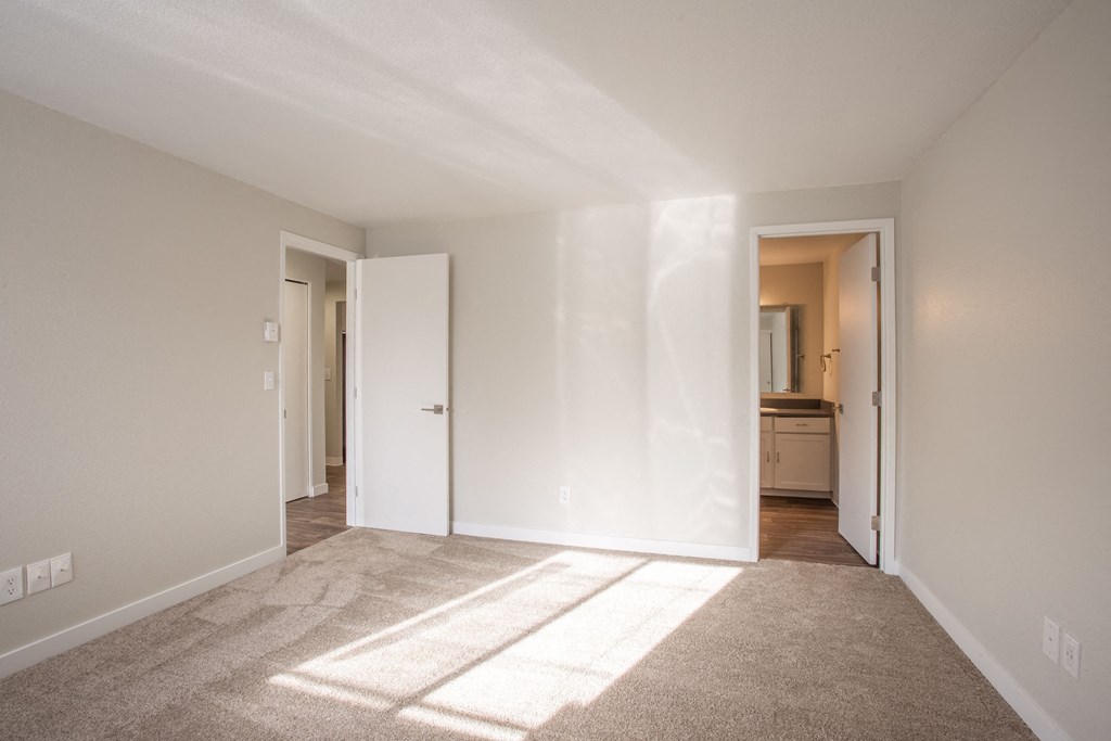 a living room with white walls and carpet and a door to a bathroom
