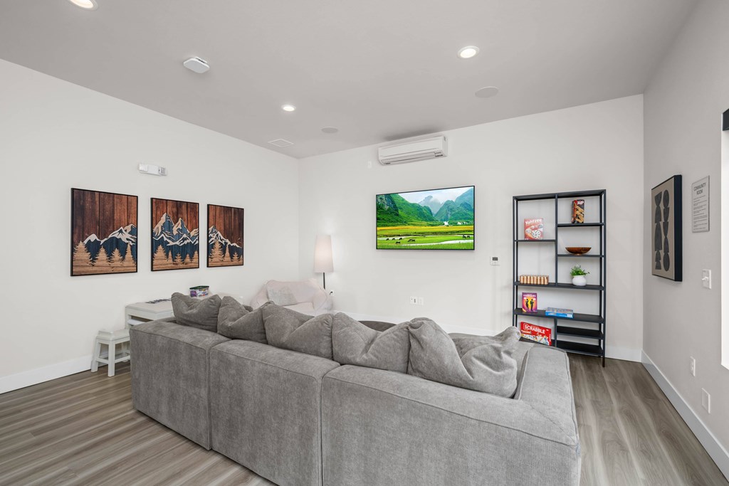 A living room with a grey couch and a painting of a green landscape on the wall.