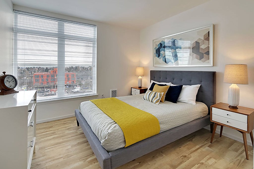 A bedroom with a bed, nightstand, and window with blinds.