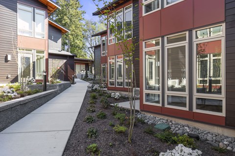 A long concrete walkway leads between two buildings with windows and plants on either side.